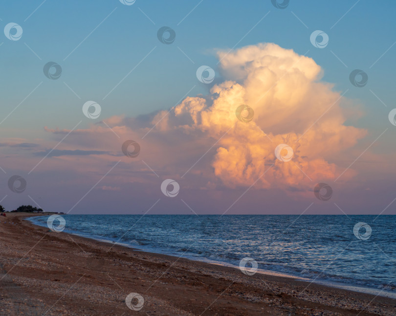 Скачать Beautiful cloudy landscape over the beach and the sea at sunset.  A huge multicolored cloud in the shape of a tunnel at sunset. An original beautiful cloud over the water and sandy beach фотосток Ozero