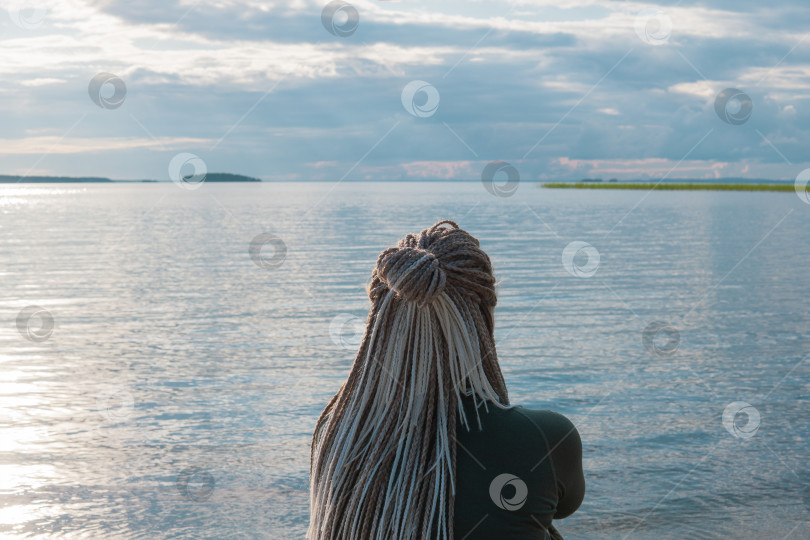 Скачать woman traveler with de braids hairstyle sitting on a sandy shore of a vast lake фотосток Ozero