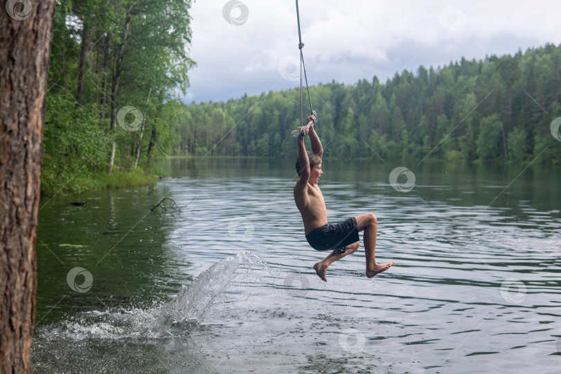 Скачать boy jumps into the water using a tarzan swing while swimming in a forest lake фотосток Ozero