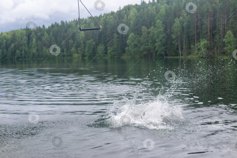 Скачать splash on the water - a bather dived into a forest lake from a makeshift tarzan swing фотосток Ozero