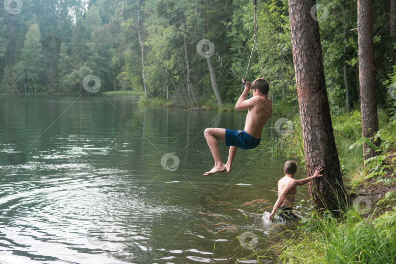 Скачать boys jumps into the water using a tarzan swing while swimming in a forest lake фотосток Ozero