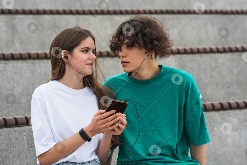 Скачать young couple together listening to the same music through headphones, sitting in empty stands фотосток Ozero