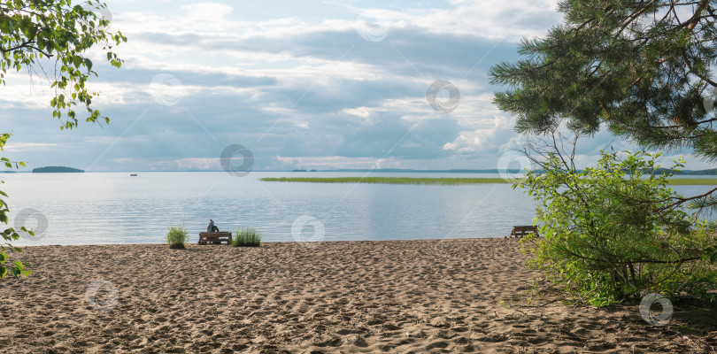 Скачать sandy beach on the shore of a vast lake, a female tourist is sitting on a bench made of old pallets фотосток Ozero