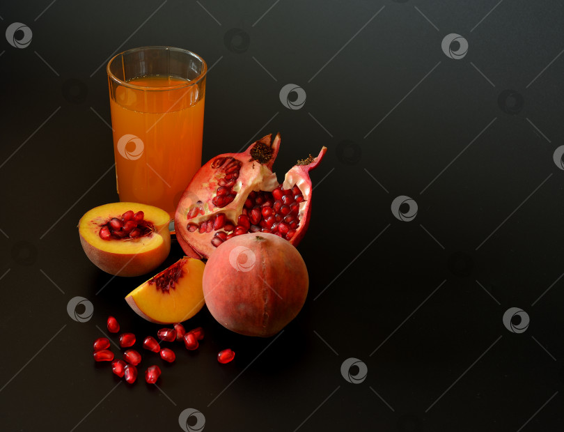 Скачать Peach-pomegranate juice in a tall glass and ripe fruits on a black background. фотосток Ozero