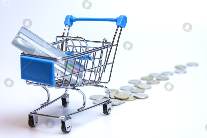 Скачать A supermarket cart on a white background with a trail of coins and a credit card. фотосток Ozero