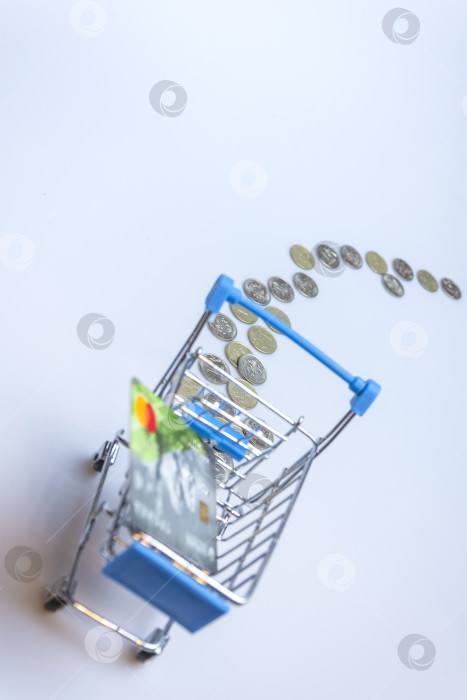 Скачать A supermarket cart on a white background with a trail of coins and a credit card. фотосток Ozero