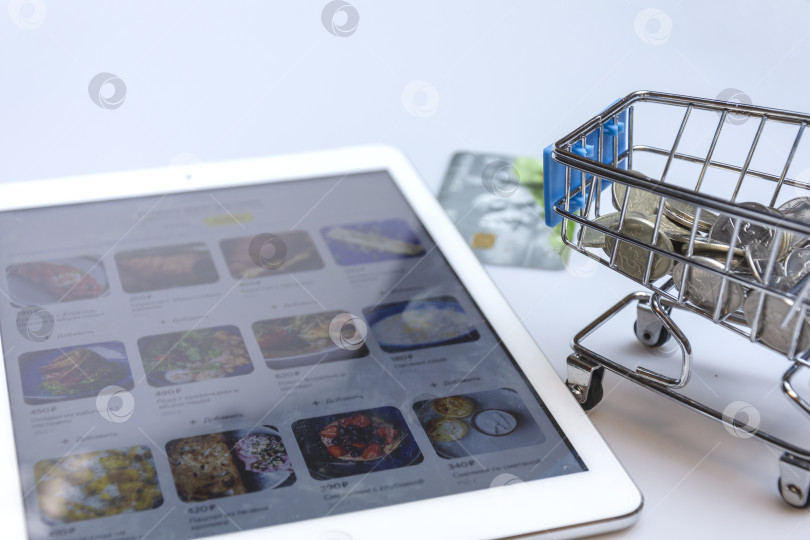 Скачать A supermarket cart with a credit card on the background of a tablet screen with an image of an online store. фотосток Ozero