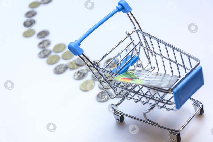 Скачать A supermarket cart on a white background with a trail of coins and a credit card. фотосток Ozero