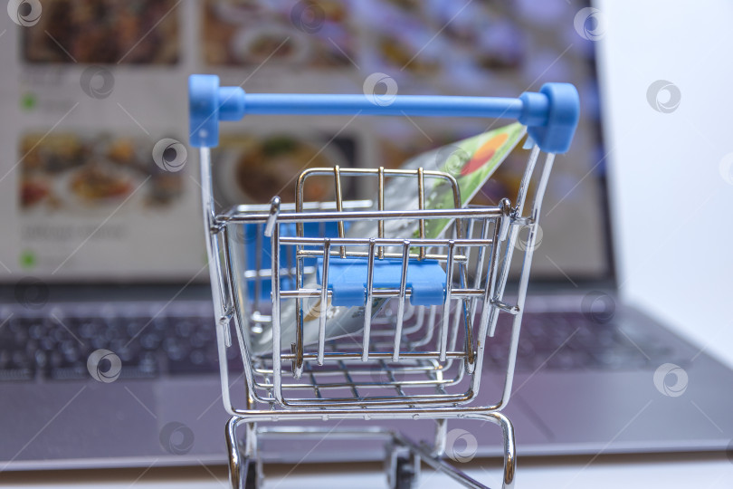 Скачать A supermarket cart with a credit card on the background of a laptop screen with an image of an online store. фотосток Ozero