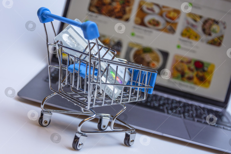 Скачать A supermarket cart with a credit card on the background of a laptop screen with an image of an online store. фотосток Ozero