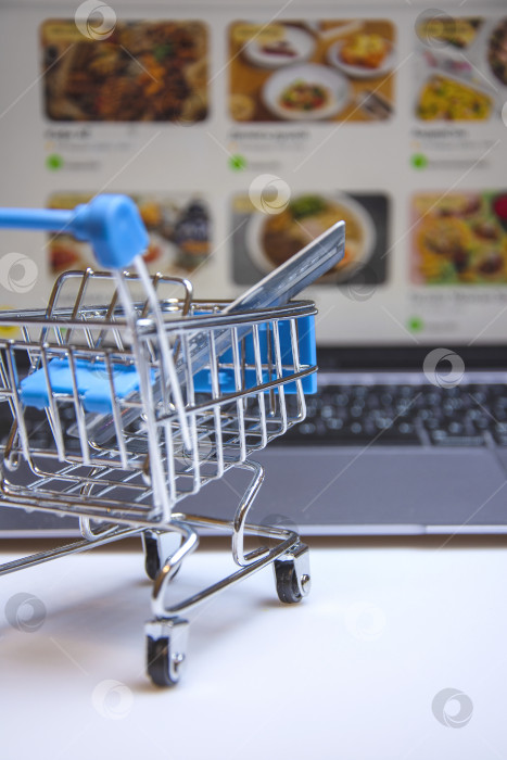 Скачать A supermarket cart with a credit card on the background of a laptop screen with an image of an online store. фотосток Ozero