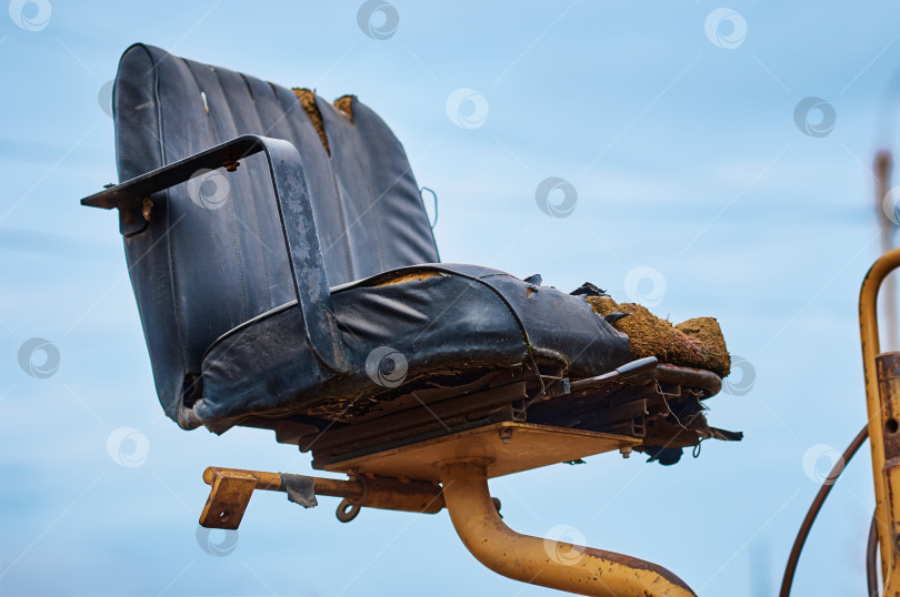 Скачать Damaged old paver operator chair against blue sky outdoors. фотосток Ozero