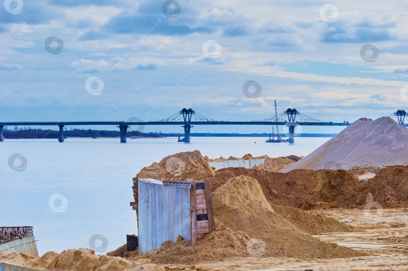 Скачать Construction site of the Zeya river embankment. Concrete dams and heaps of sand against the backdrop of a road bridge under construction. фотосток Ozero