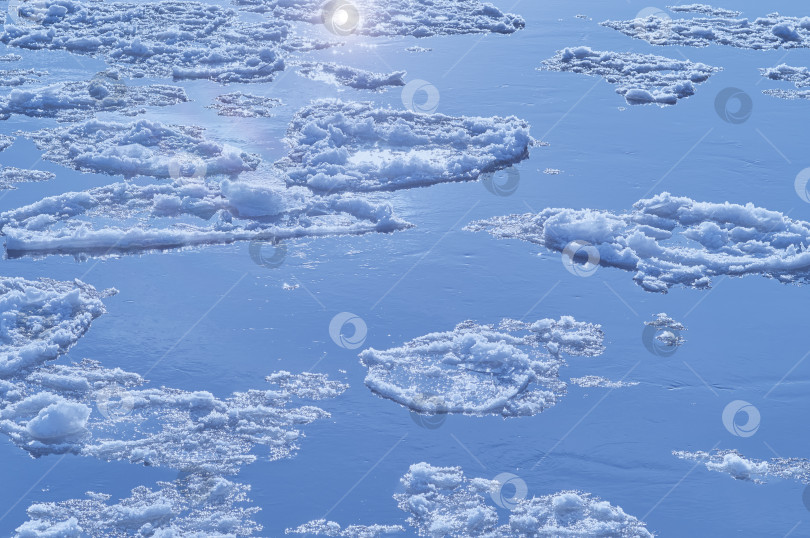 Скачать Ice floes float on the river. Seasonal ice drift. Reflection of the blue sky in the water фотосток Ozero