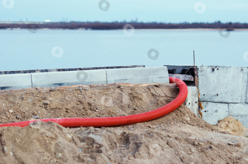 Скачать A red corrugated pipe for laying an electrical cable sticks out of the ground at a construction site. Curb stones are installed in a row using formwork and liquid concrete. фотосток Ozero