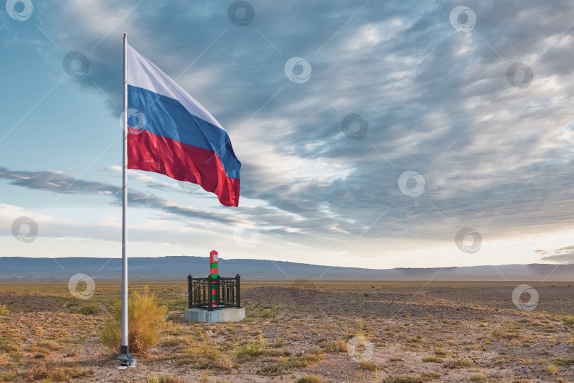 Скачать The flag of the Russian Federation is set on a flagpole in the steppe. Clouds in the sky. фотосток Ozero