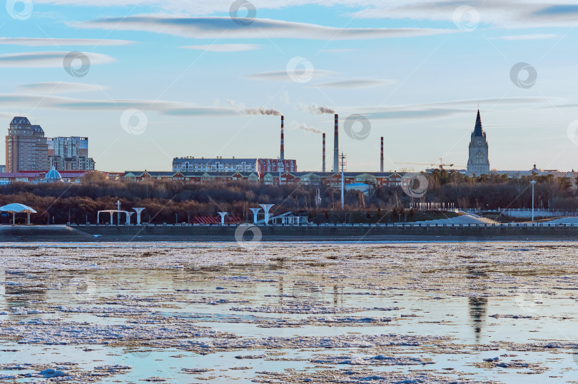 Скачать Evening landscape on the river during ice drift with strange clouds. View of the coast of China from Russia. Residential and administrative buildings, chimneys and church. фотосток Ozero