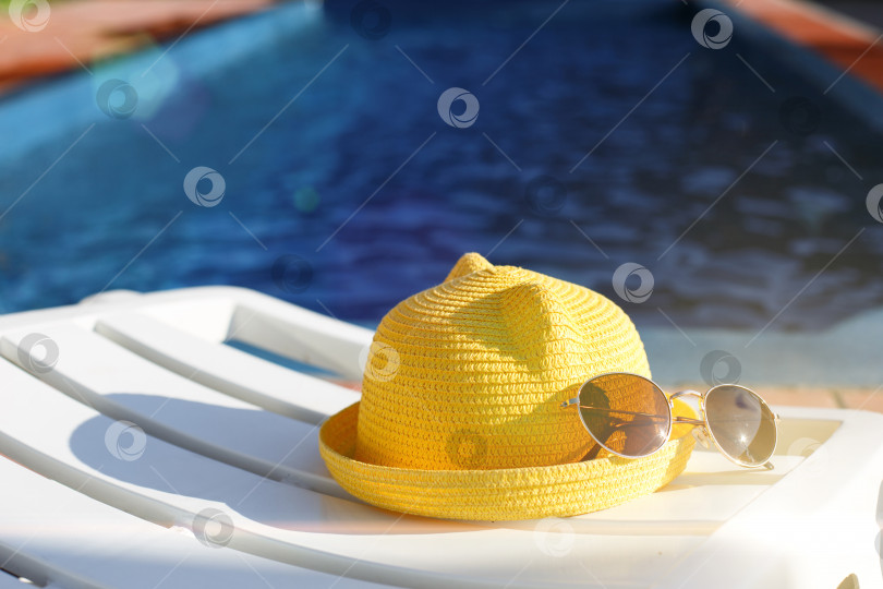 Скачать Пляжные принадлежности желтая шляпа и солнцезащитные очки лежат на белом шезлонге у бассейна. Защита от солнца, ультрафиолет, загар, путешествия. Концепция отпуска, морская прогулка, плавание. Пространство для копирования. Плоский лист фотосток Ozero