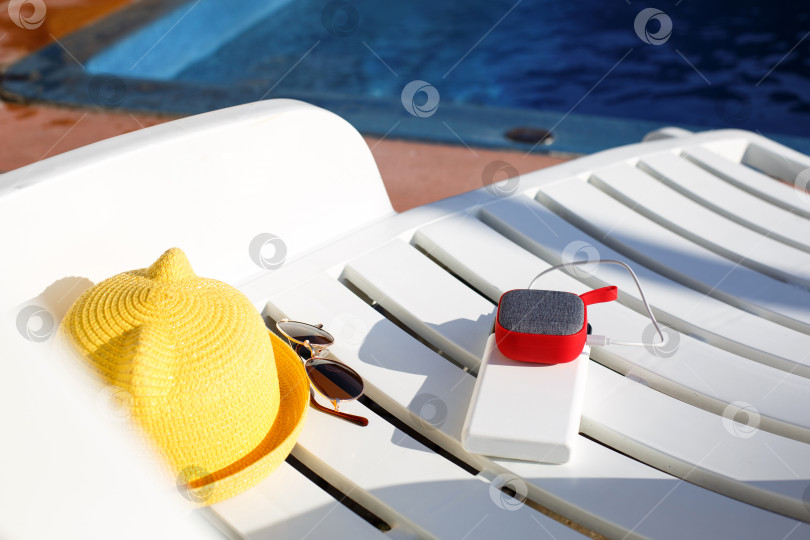 Скачать Музыкальный портативный динамик заряжается от блока питания через usb на шезлонге у бассейна с пляжными принадлежностями. Всегда на связи, гаджеты для путешествий, внешний аккумулятор для смартфона. Место для текста. Плоский лист фотосток Ozero