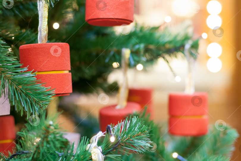 Скачать Close-up view of a Christmas tree decoration, in the shape of a red cylinder with blurred lights in bokeh on a background (copy space) фотосток Ozero