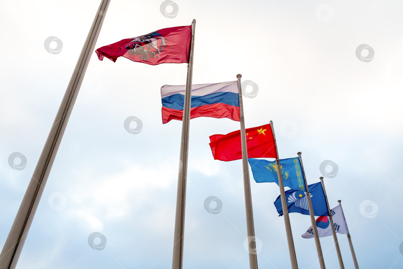 Скачать View on the flags of China, Kazakhstan, South Korea, Russia, Commonwealth of Independent States, coat of arms of Moscow on the background of cloudy sky фотосток Ozero
