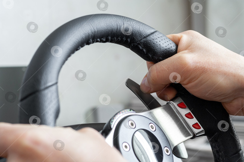 Скачать View on a man's hands playing a racing simulator on a steering wheel фотосток Ozero