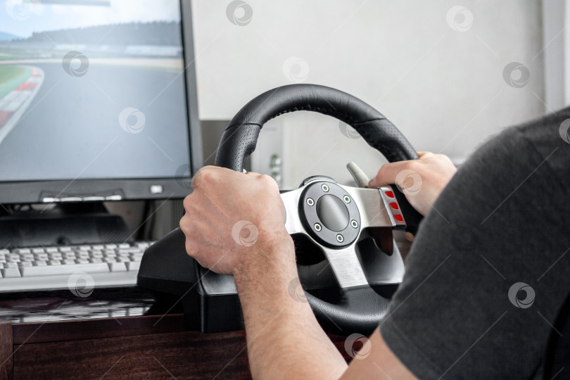 Скачать View on a man's hands playing a racing simulator on a steering wheel фотосток Ozero