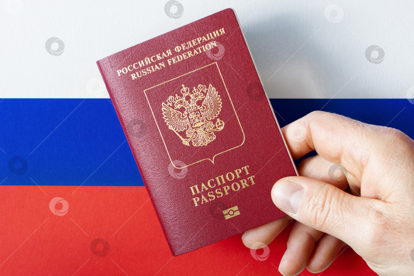 Скачать A man's hand holds a International passport of the Russian Federation on a background of national flag фотосток Ozero