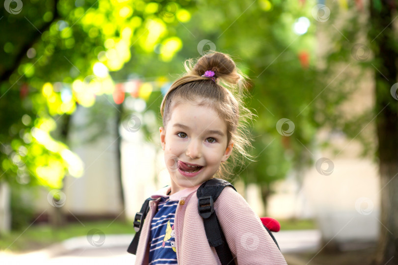 Скачать В кадр заглядывает маленькая девочка кавказской внешности в школьной форме с рюкзаком. Концепция возвращения в школу. Начальная школа, развивающие занятия для дошкольников. Пространство для текста фотосток Ozero