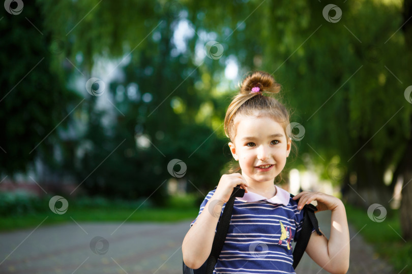 Скачать В кадр заглядывает маленькая девочка кавказской внешности в школьной форме с рюкзаком. Концепция возвращения в школу. Первый класс, развивающие занятия для дошкольников. Пространство для текста фотосток Ozero