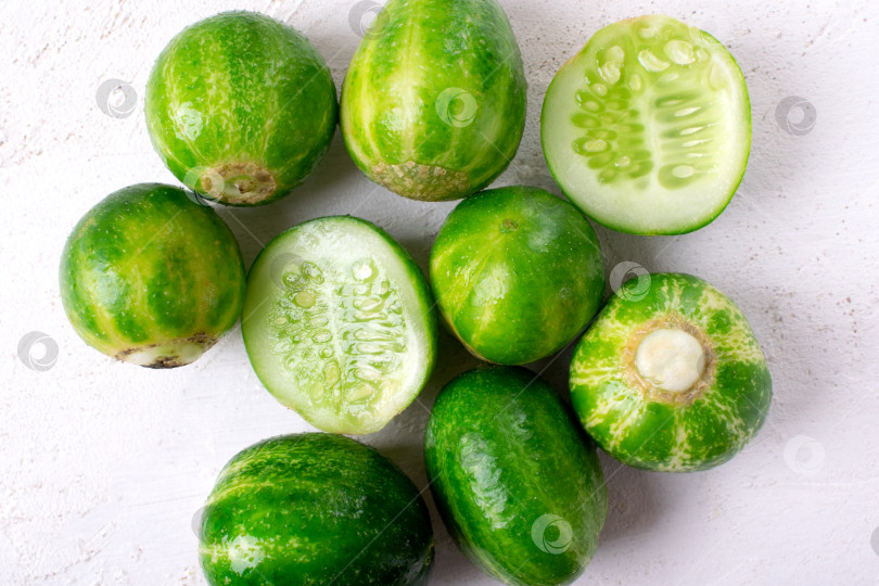 Скачать Small round cucumbers with stripes reminding watermelon on white table. фотосток Ozero