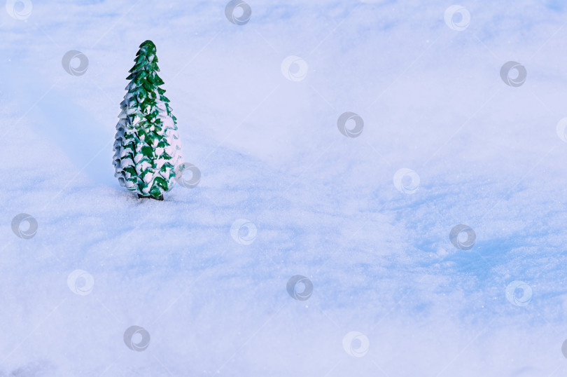 Скачать Игрушечная фигурка рождественской елки стоит на естественной заснеженной поверхности на открытом воздухе. Отражения вечернего солнца на снежинках. Рождественский фон. фотосток Ozero