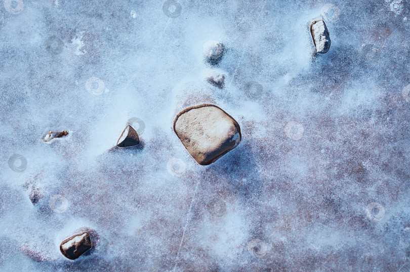 Скачать Округлые камни, вмерзшие в лед на берегах Амура, греются на солнце и оттаивают. Крупный план, вид сверху. Естественный абстрактный текстурный фон. Пространство для копирования. фотосток Ozero