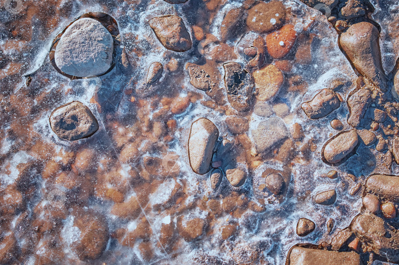 Скачать Округлые камни, вмерзшие в лед на берегах Амура, греются на солнце и оттаивают. Крупный план, вид сверху. фотосток Ozero