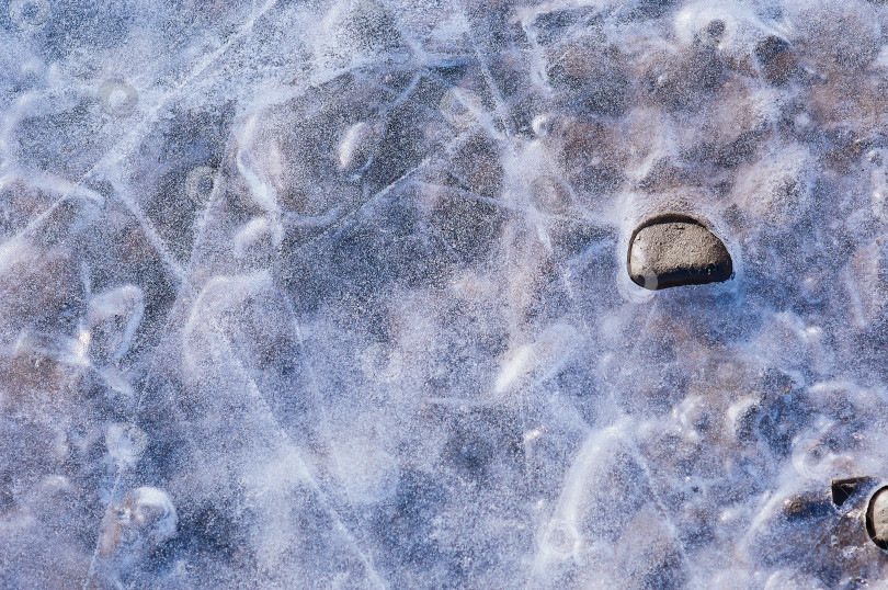 Скачать Камни, вмерзшие в лед на берегах Амура, греются на солнце и оттаивают. Крупный план, вид сверху. фотосток Ozero