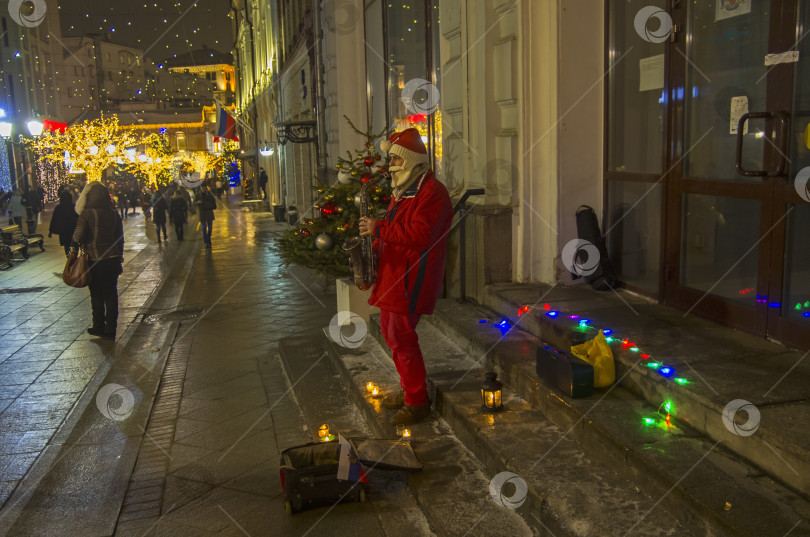 Скачать Уличный музыкант в костюме Санта-Клауса играет на саксофоне фотосток Ozero