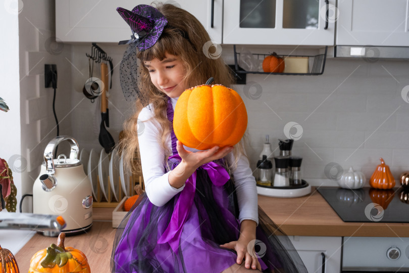 Скачать Ребенок украшает кухню дома к Хэллоуину. Девочка в костюме ведьмы играет с декором для праздника - летучими мышами, фонарем Джека, тыквами. Осенний уют в доме, кухня в стиле Сканди, лофт фотосток Ozero