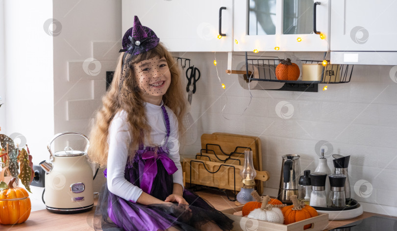 Скачать Ребенок украшает кухню дома к Хэллоуину. Девочка в костюме ведьмы играет с декором для праздника - летучими мышами, фонарем Джека, тыквами. Осенний уют в доме, кухня в стиле Сканди, лофт фотосток Ozero