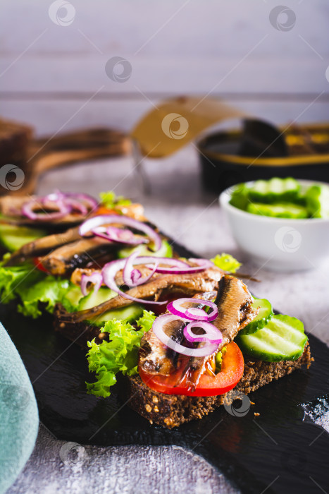 Скачать Бутерброды на ржаном хлебе с помидорами, огурцами, шпротами и луком на грифельной доске вертикальный вид фотосток Ozero