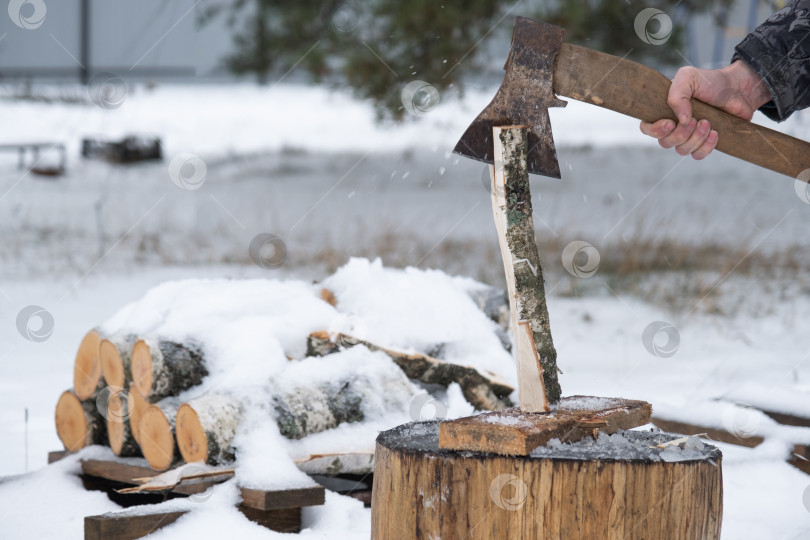 Скачать Мужчина рубит топором дрова зимой на открытом воздухе в снегу. Альтернативное отопление, заготовка древесины, энергетический кризис фотосток Ozero