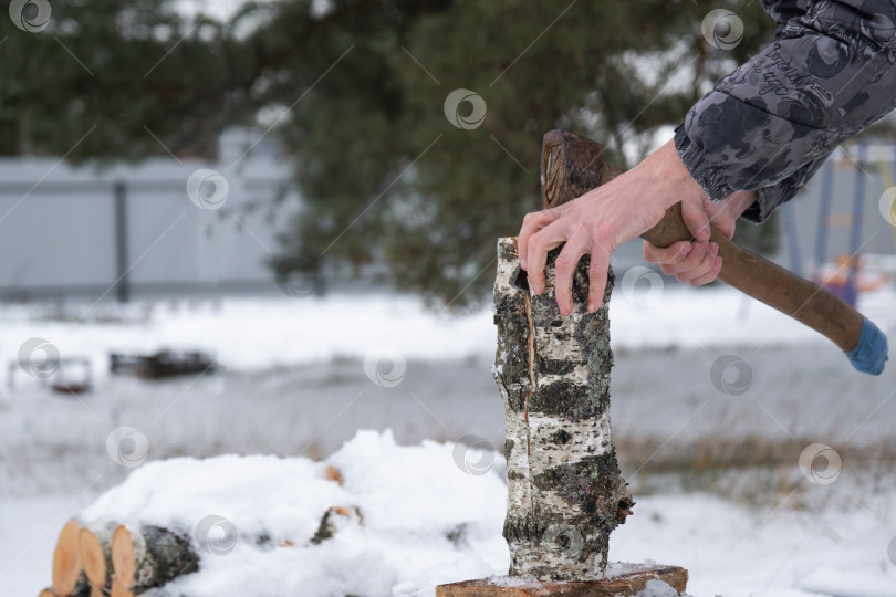Скачать Мужчина рубит топором дрова зимой на открытом воздухе, в снегу. Альтернативное отопление, заготовка древесины, энергетический кризис фотосток Ozero