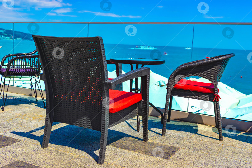 Скачать Пустая мебель из ротанга, стулья, столик в летнем уличном кафе на берегу моря в Крыму, хорошее место, чтобы выпить кофе с видом на морское побережье, корабли, небо. фотосток Ozero
