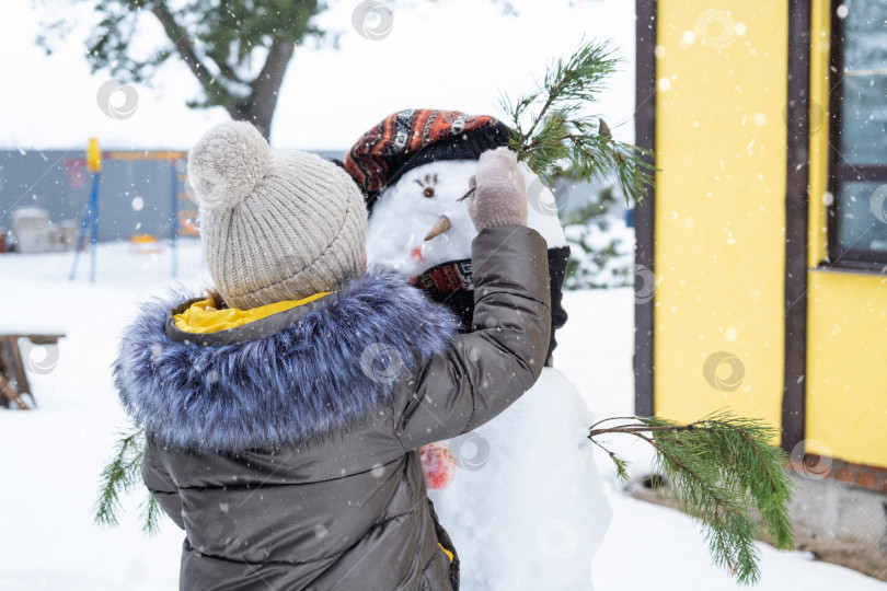 Скачать Ребенок раскрашивает лицо снеговика красками - зимнее развлечение и творчество, лепка снеговика зимой на открытом воздухе. фотосток Ozero
