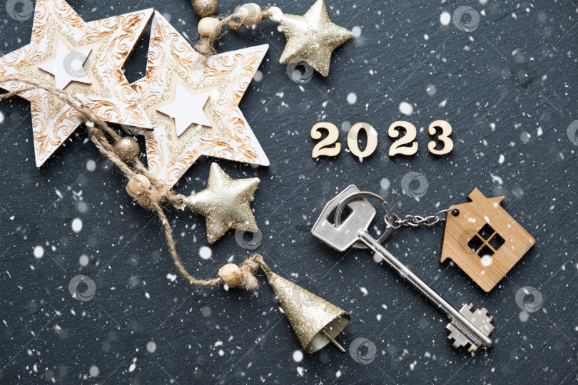 Скачать Ключ от дома с брелком для ключей коттедж на черном фоне со звездами, снежинками. С Новым 2023 годом -деревянные буквы, поздравительная открытка. Покупка, строительство, переезд, ипотека фотосток Ozero