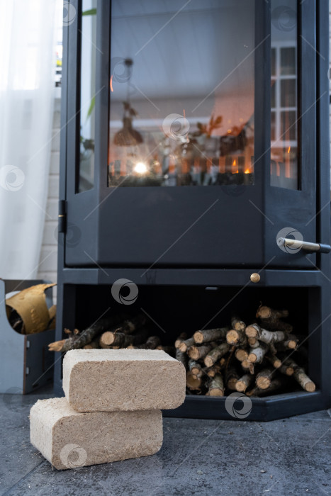 Скачать Топливные брикеты из прессованных опилок для растопки печи - экономичная альтернатива экологически чистому топливу для камина в доме. Внутри в печи горят дрова фотосток Ozero