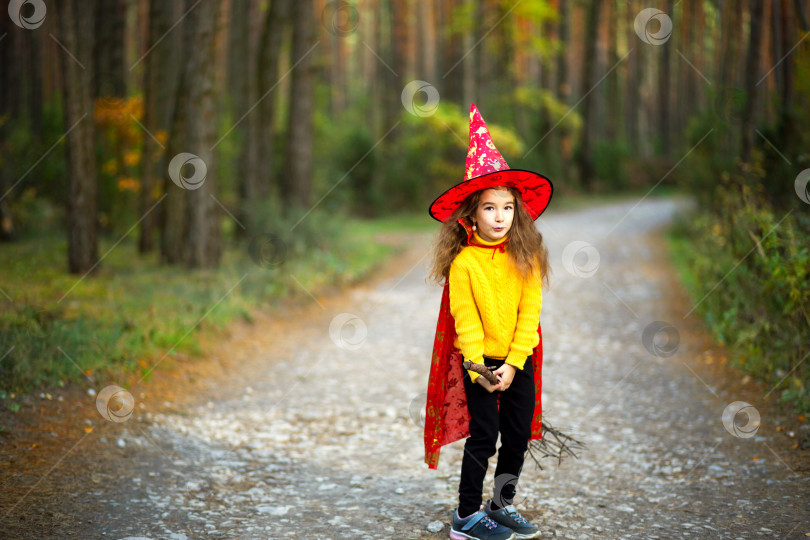 Скачать Девочка в костюме ведьмы и шляпе на метле играет в осеннем лесу, собираясь на вечеринку в честь Хэллоуина фотосток Ozero