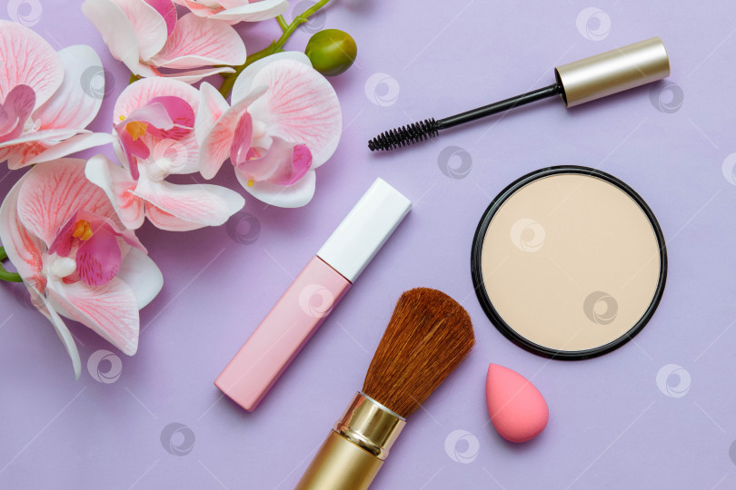 Скачать decorative cosmetics mascara, lipstick, powder, sponge and bone on a pink background with orchid flowers фотосток Ozero