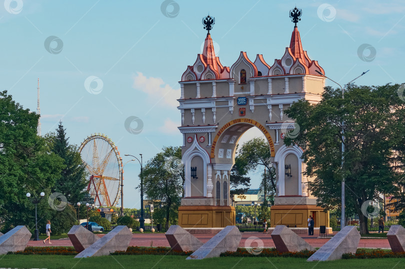 Скачать Triumphal arch to a sunny evening. Blagoveshchensk, Far East, Russia. Ferris wheel in the background on the Chinese bank of the Amur River. фотосток Ozero