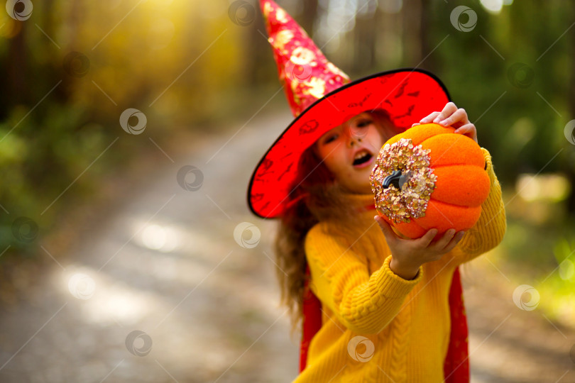 Скачать Девушка в шляпе ведьмы, в желтом свитере и с тыквой с вырезанными глазами и ртом Джек о Фонарь в желтом осеннем лесу. Праздник Хэллоуина фотосток Ozero