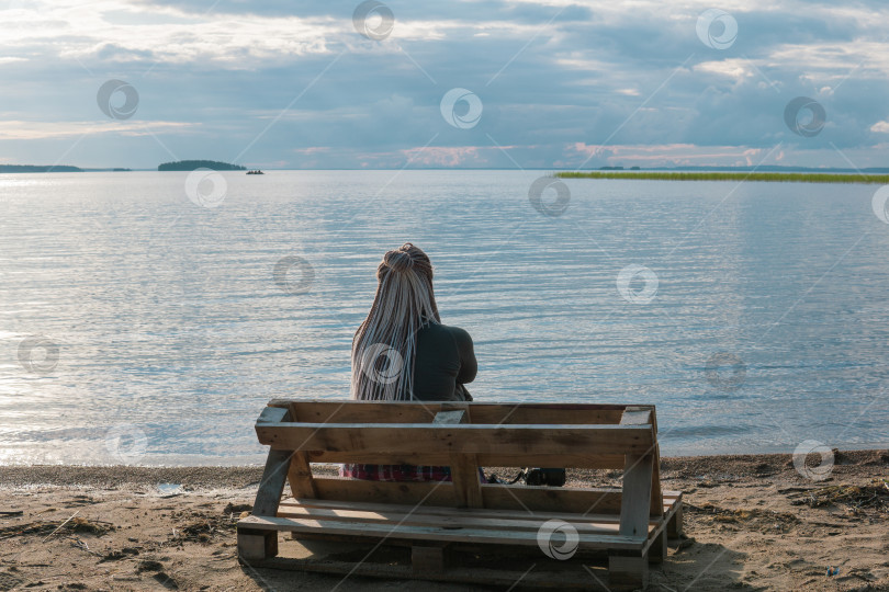 Скачать песчаный пляж на берегу огромного озера, женщина-путешественница сидит на скамейке, сделанной из старых поддонов фотосток Ozero